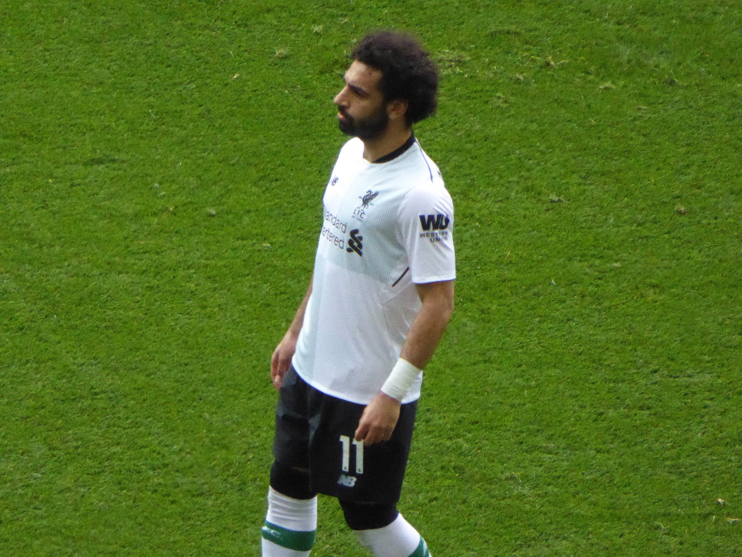Mohamed Salah standing on the pitch in Liverpool's white away shirt in 2018.