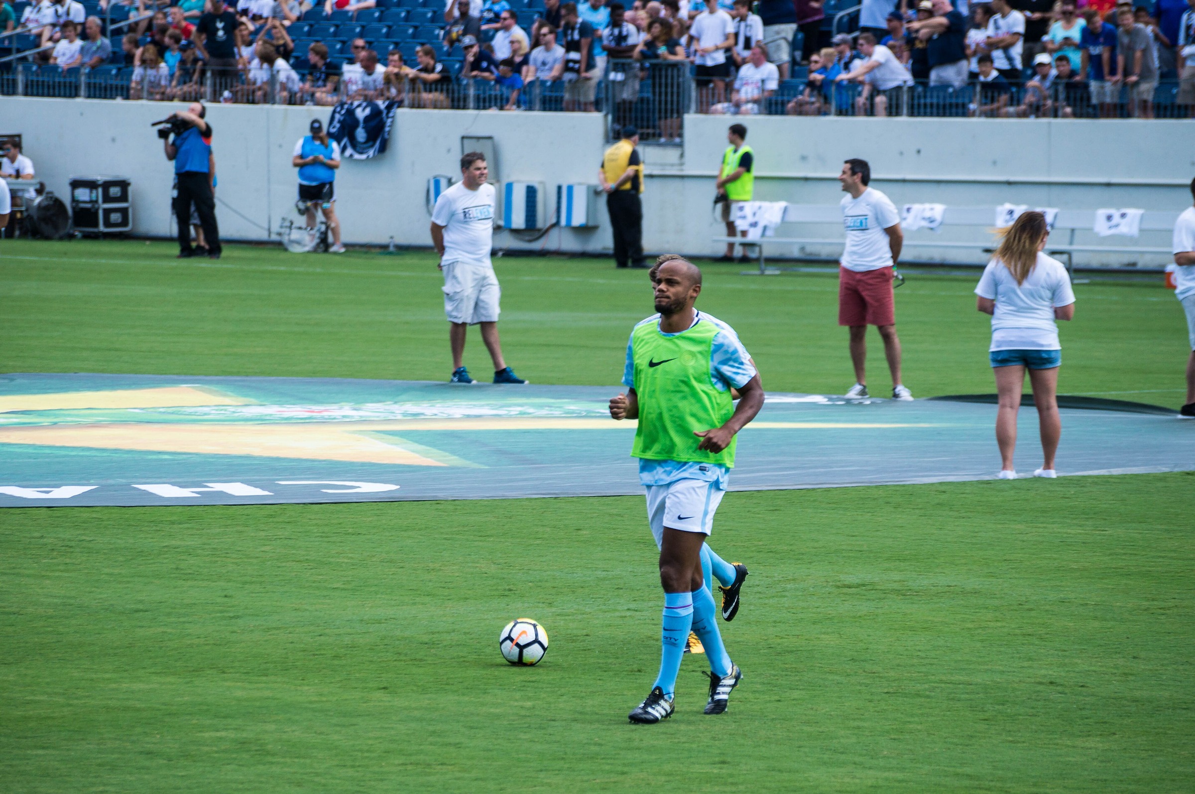 Vincent Kompany warming up in a green bib and Manchester City training kit on a football pitch in 2017.